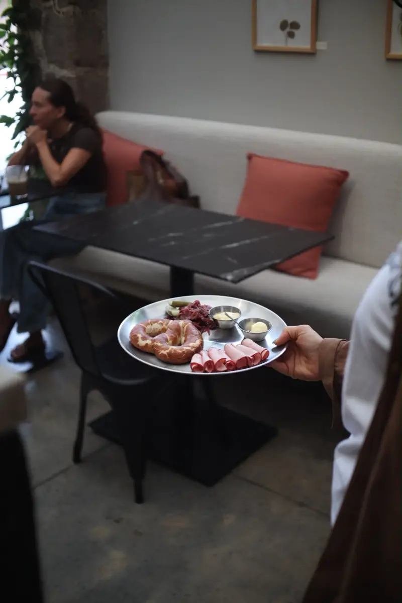 Servicio en Haramara: plato de acero con pretzel y encurtidos llevado a una mesa de mármol negro