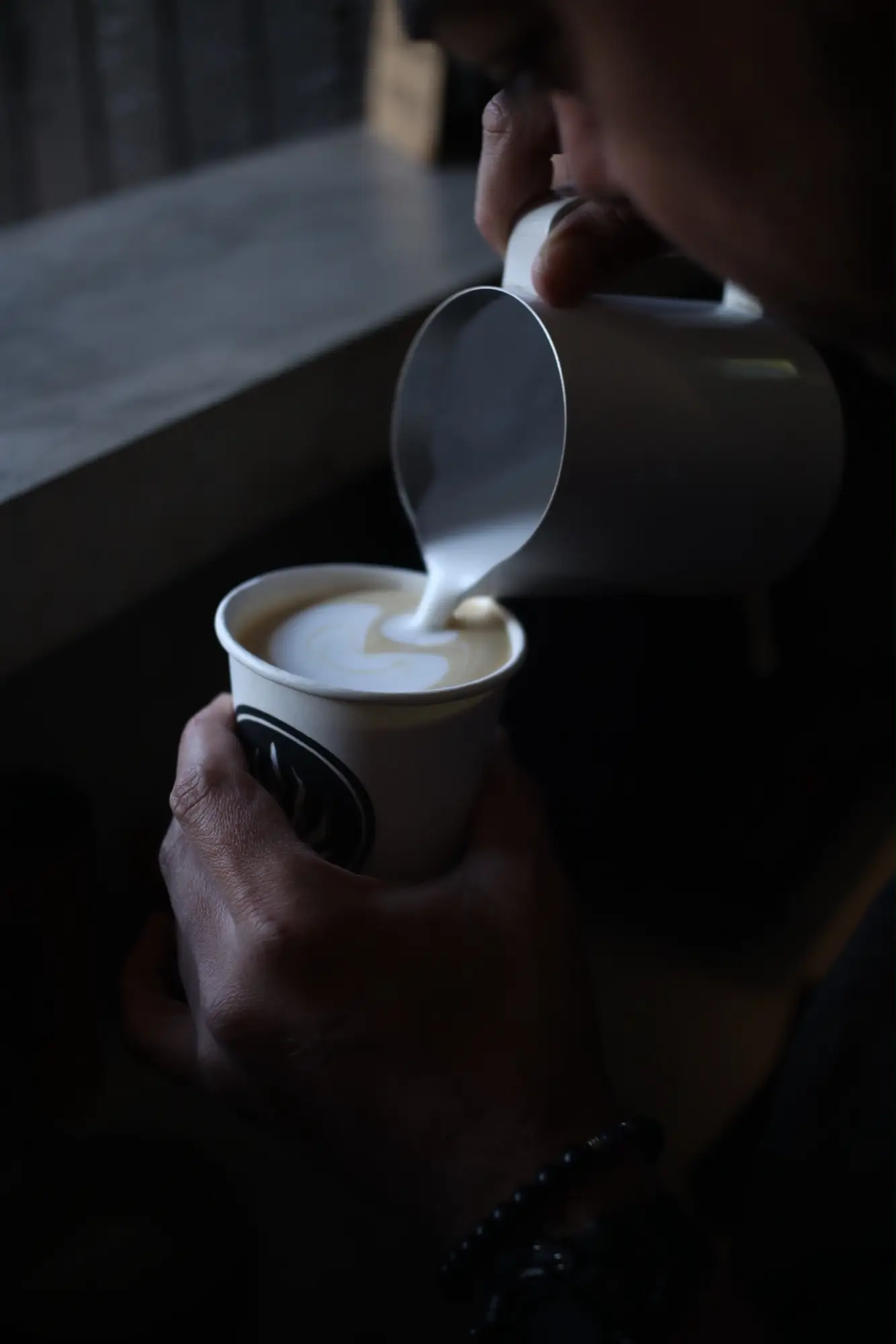Barista de Haramara vertiendo leche sobre un café en la penumbra de la barra