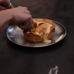 Crème brûlée sobre laminado, servida en plato de acero y rota con cuchara.