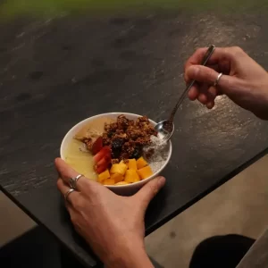 Bowl de pudding de chía con mango, fresa, kiwi y granola sobre mesa de piedra negra.